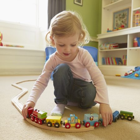 Female toddler playing with toy train on playroom floor