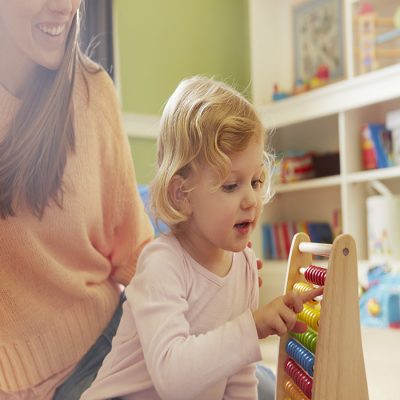 Mid adult woman and toddler daughter counting on abacus in playroom